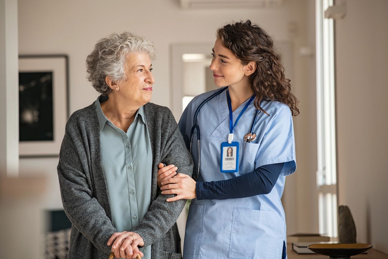 Young caregiver helping senior woman walking. Nurse assisting her old woman patient at nursing home. Senior woman with walking stick being helped by nurse at home. (Young caregiver helping senior woman walking. Nurse assisting her old woman patient at