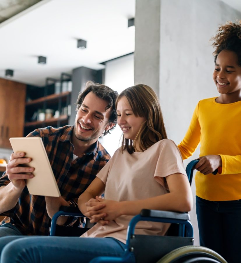 Happy multiethnic family with disabled child in wheelchair playing together at home